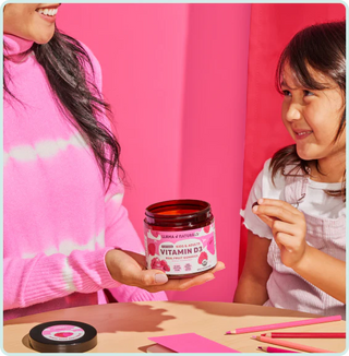 Two people holding a jar of vitamin D3 supplement against a pink background