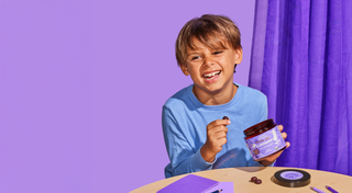 Child holding a jar of purple cream against a purple background