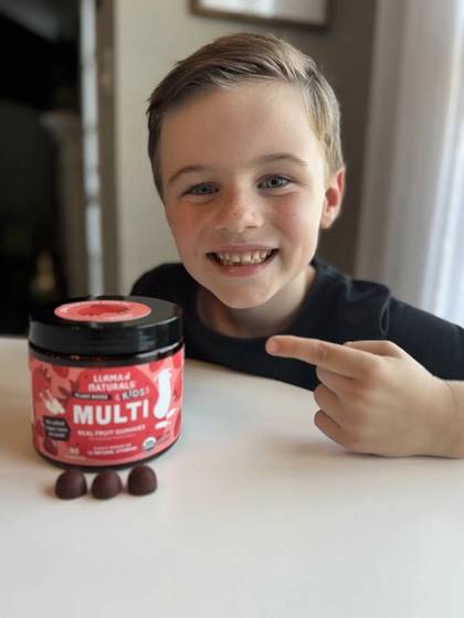 A smiling child pointing to a Kids Multi jar beside gummies.