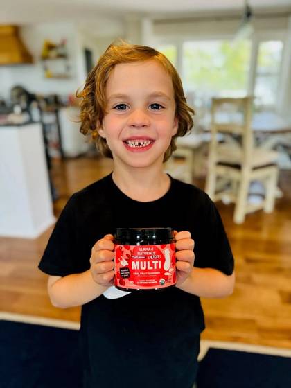 A smiling child holding a Kids Multi jar in the kitchen.