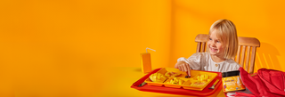Child sitting at a table with a tray of food against an orange background