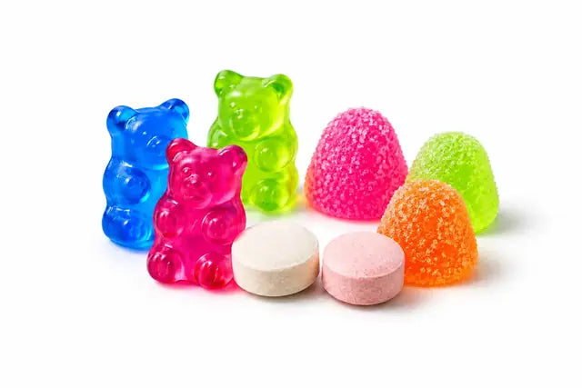 Illustrative neon gummy bears, two round chalky chewable tablets and sugar-coated gumdrops on white
