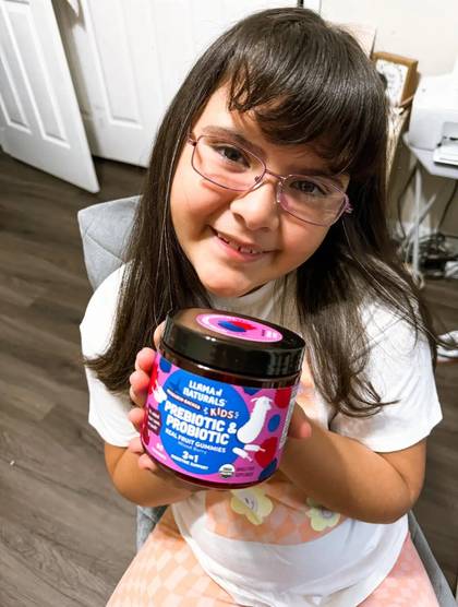 A smiling child with glasses holding a Kids Digestion jar.