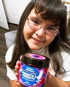 A smiling child with glasses holding a Kids Digestion jar.