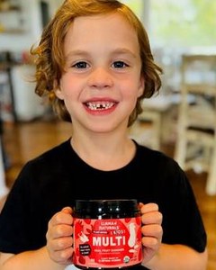A smiling child holding a Kids Multi jar in the kitchen.